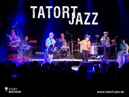 Die Künstlergruppe spielt ihr Stück auf einer Bühne vor Publikum.