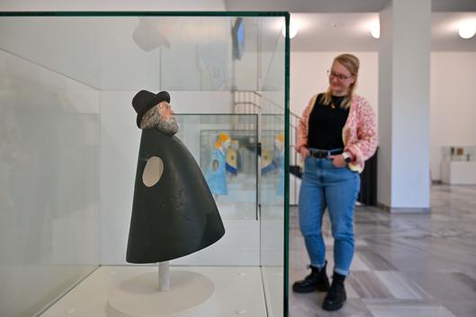 Eine Frau schaut sich die Ausstellungsstücke in den Vitrinen an. Im Vordergrund ist eine Figur zu sehen.