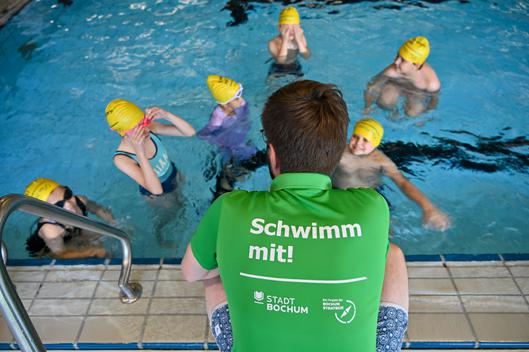 Es ist ein Mann von hinten zu sehen, der mit den Kindern im Wasser spricht.