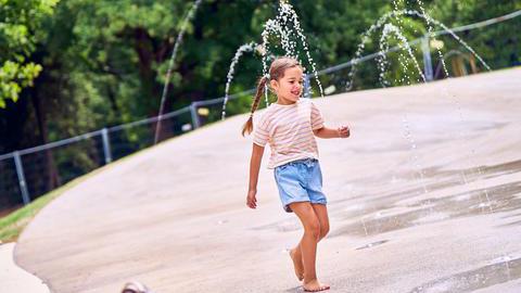 Ein Mädchen spielt auf einem Wasserspielplatz.
