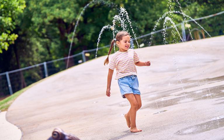 Ein Mädchen spielt auf einem Wasserspielplatz.