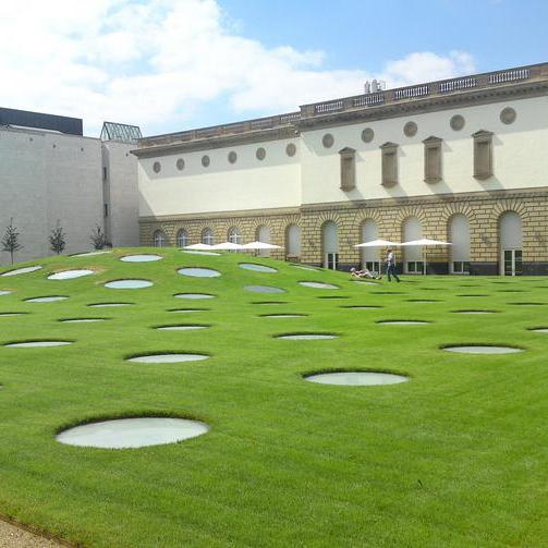 Ein begrünter Innenhof zwischen modernen Campus-Gebäuden mit geschwungenen Wegen, Rasenflächen und jungen Bäumen.