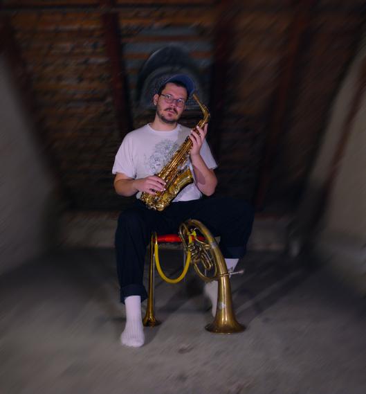 Felix Nussbaumer sitzt auf einem Stuhl und hält ein Saxophon in der Hand