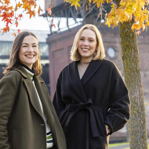 Zwei junge Frauen stehen im Herbstwetter vor der Jahrhunderthalle in Bochum.