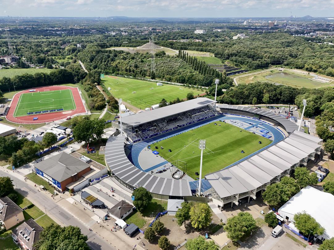 Luftaufnahme des Lohrheidestadions mit blauer Tartanbahn, Tribünen und umliegenden Grünflächen.