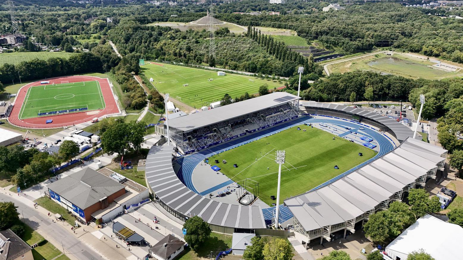 Luftaufnahme des Lohrheidestadions mit blauer Tartanbahn, Tribünen und umliegenden Grünflächen.
