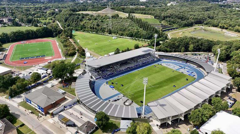 Luftaufnahme des Lohrheidestadions mit blauer Tartanbahn, Tribünen und umliegenden Grünflächen.