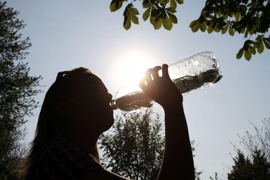 Eine Frau trinkt aus einer Wasserflasche bei strahlendem Sonnenschein.
