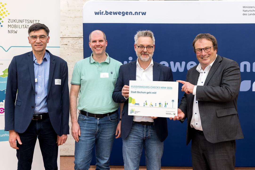 Vier Personen lachen in die Kamera und präsentieren eine Urkunde.