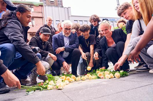 Personen legen Rosen an der neuen Stolperschwelle nieder