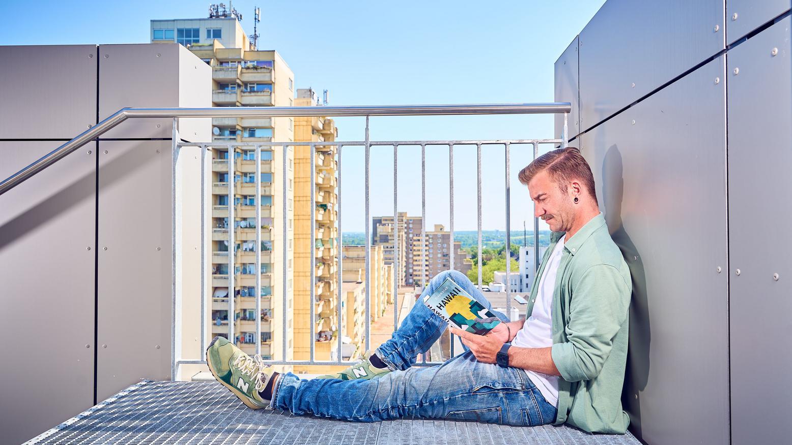 Ein Mann sitzt an einer Treppe und liest das Buch "Hawaii"