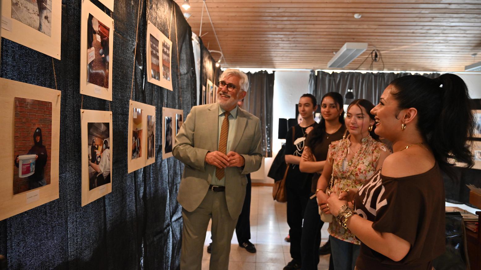 Oberbürgermeister Jörg Lukat betrachtet gemeinsam mit Besucherinnen und Besuchern die ausgestellten Fotografien einer Ausstellung.