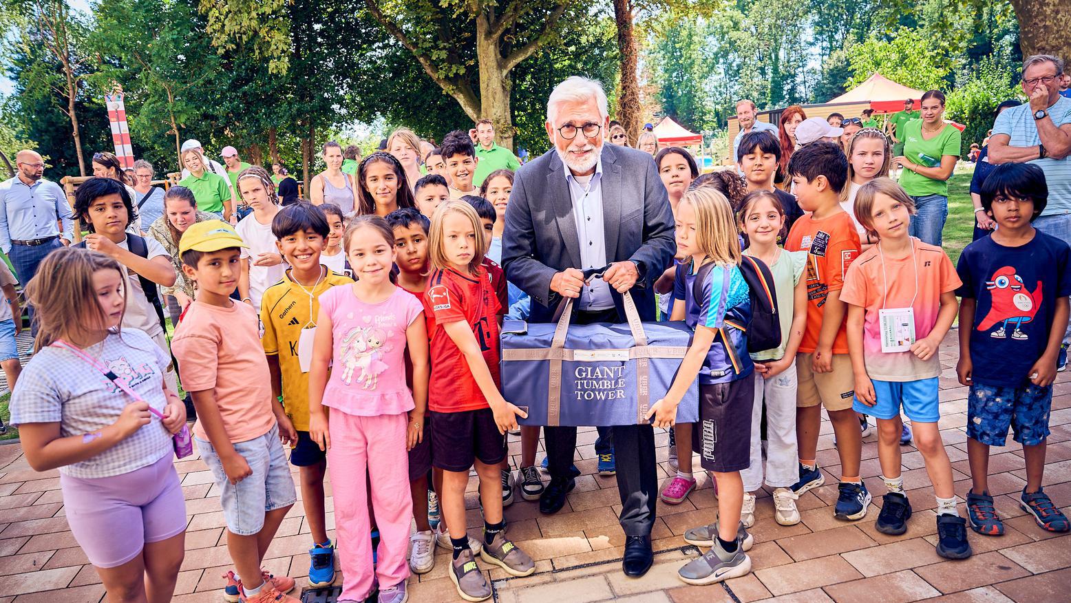 Oberbürgermeister Jörg Lukat präsentiert gemeinsam mit Kindern ein neues Spielgerät bei der Eröffnung eines Außengeländes.