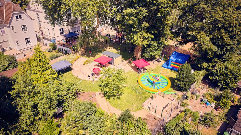 Luftaufnahme des Außengeländes mit Spiel- und Freizeitangeboten, Pavillons und zahlreichen Besucherinnen und Besuchern.