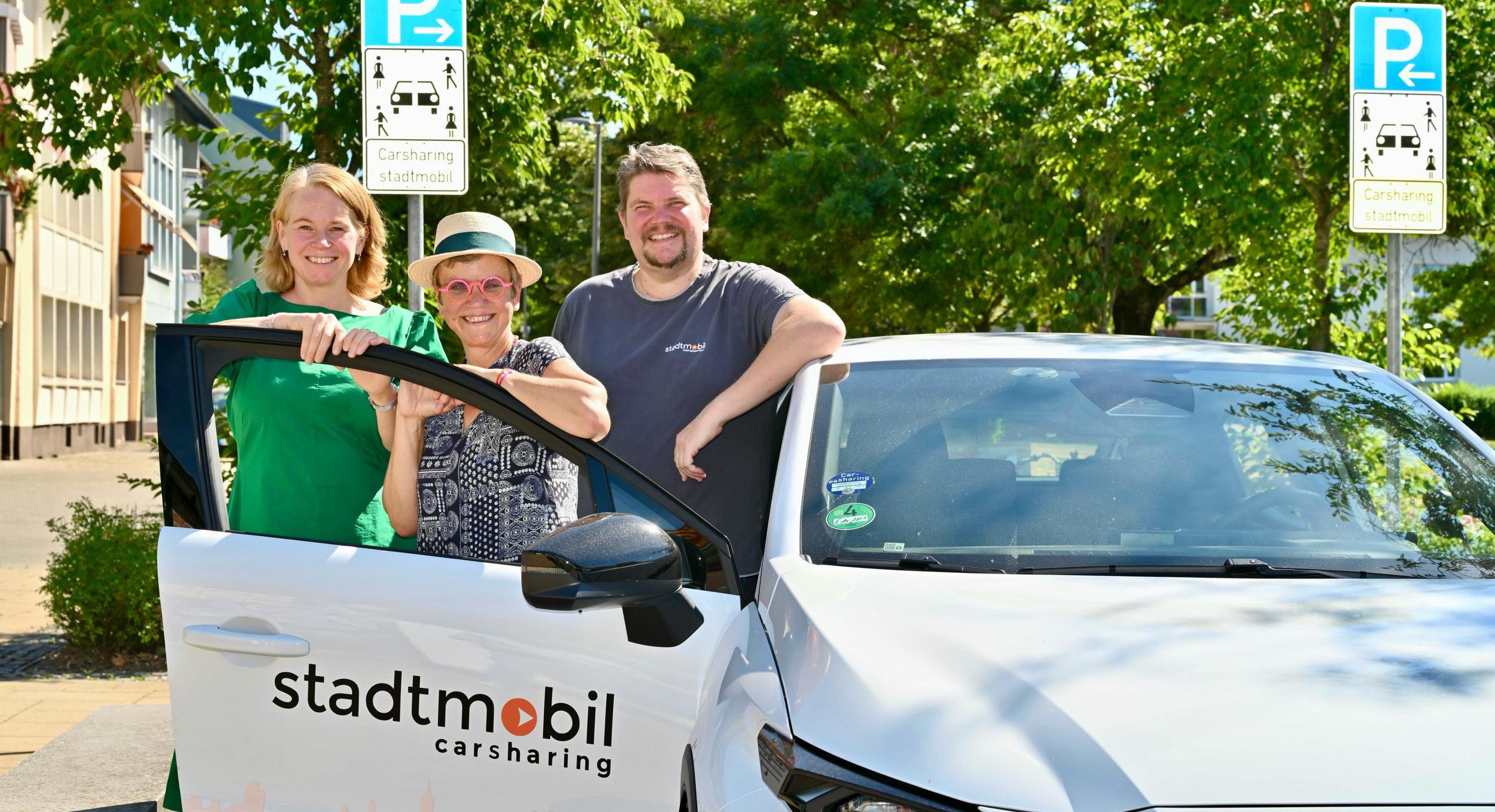 Drei Personen stehen an einem Carsharing-Fahrzeug an einem ausgewiesenen Carsharing-Stellplatz.