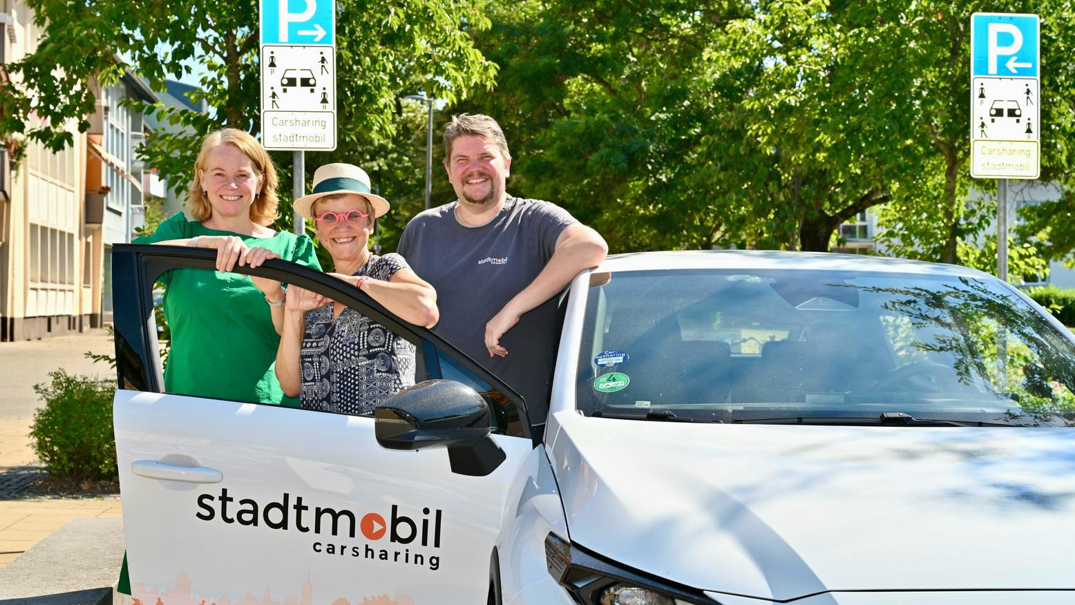 Drei Personen stehen an einem Carsharing-Fahrzeug an einem ausgewiesenen Carsharing-Stellplatz.