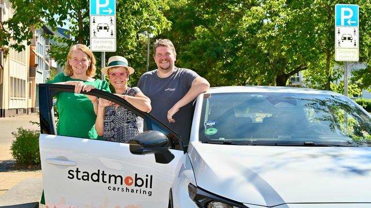 Drei Personen stehen an einem Carsharing-Fahrzeug an einem ausgewiesenen Carsharing-Stellplatz.